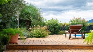 A wooden deck with a pool chair and a small table, surrounded by lush greenery and a cloudy sky. - Villa Grey - Three Bedroom Villa with Swimming pool (Kastel Kambelovac)