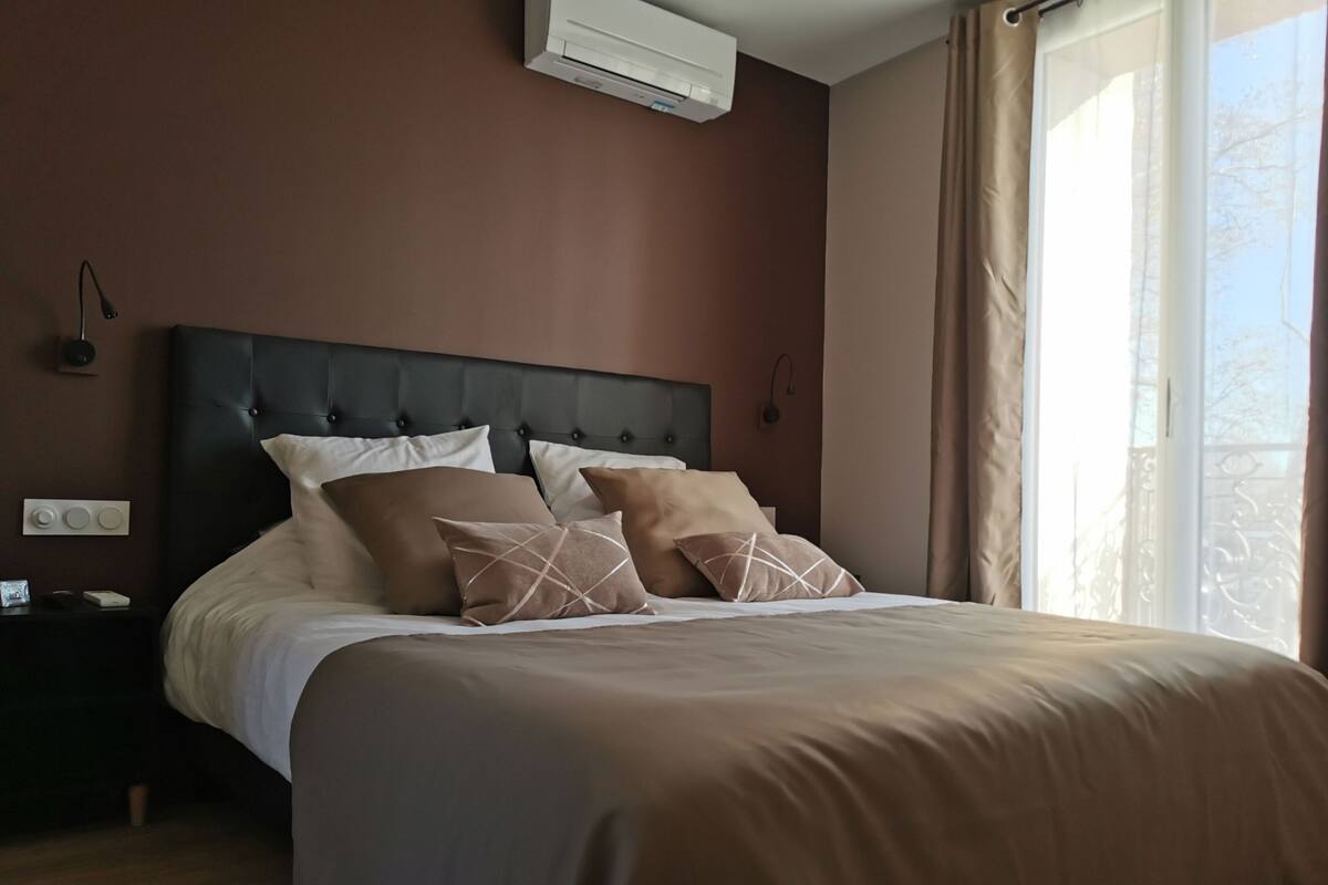A neatly made bed with a dark headboard, a bedside table with a lamp, and a window with curtains.