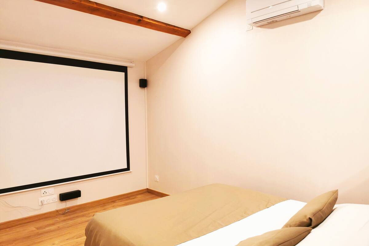 A bedroom with a bed, a projector screen, and an air conditioning unit.