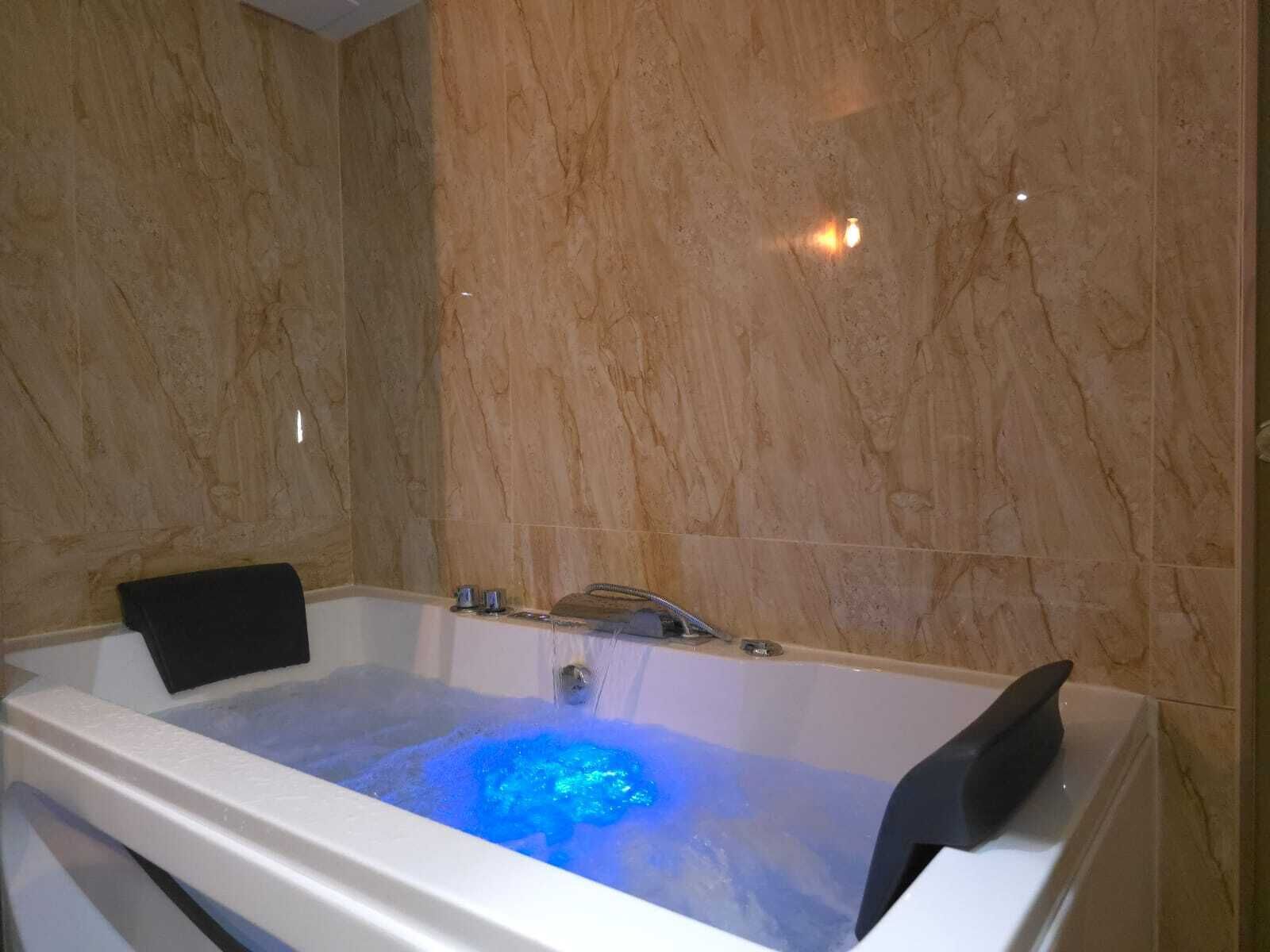 Un baño moderno con pared de mármol, bañera con luz azul y una silla negra.