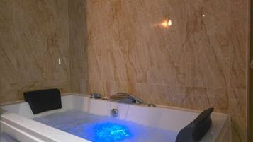 Un baño moderno con pared de mármol, bañera con luz azul y una silla negra.