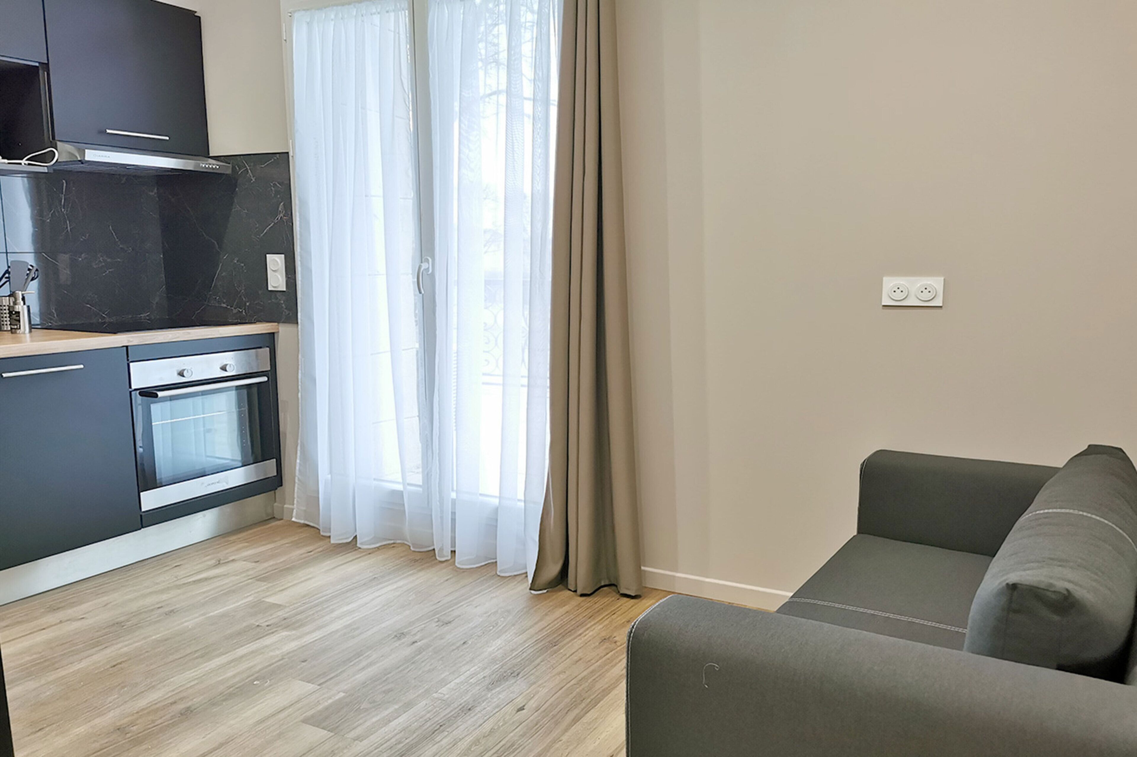 A modern kitchen with a built-in oven and a grey sofa in a living area.