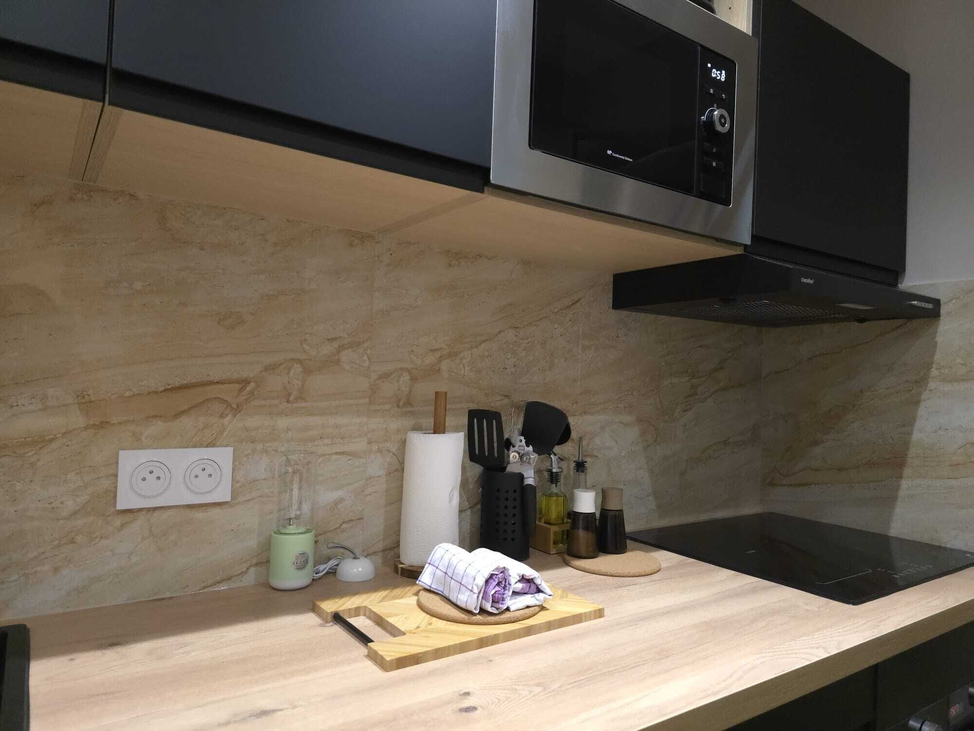 A modern kitchen with a wooden countertop, a black induction cooktop, a stainless steel microwave, and a black range hood.