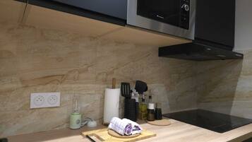 A modern kitchen with a wooden countertop, a black induction cooktop, a stainless steel microwave, and a black range hood.