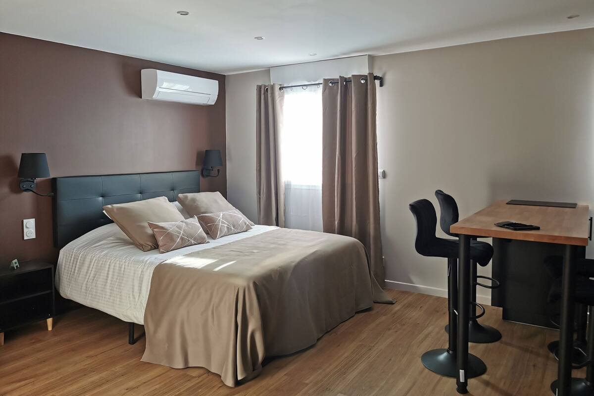 A hotel room with a bed, bedside lamps, a table with chairs, and an air conditioning unit.