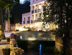 A stone bridge over a calm water body, with a building featuring balconies and outdoor lighting on the right. - Appart Hotel Spa Perpignan (Perpignan)