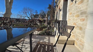 An outdoor patio with a table and chairs, a stone wall, and a view of trees and buildings in the background.