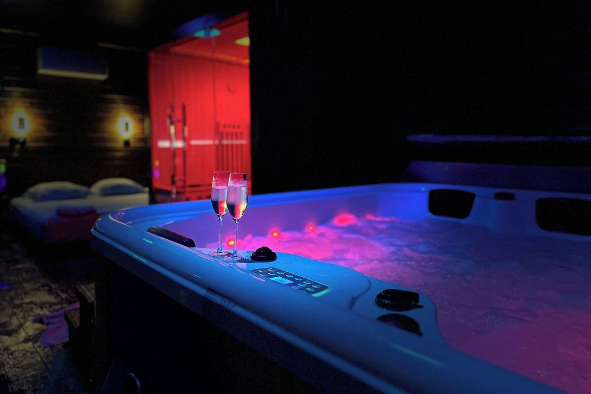 A hot tub with two glasses of champagne, a control panel, and a red-lit background.