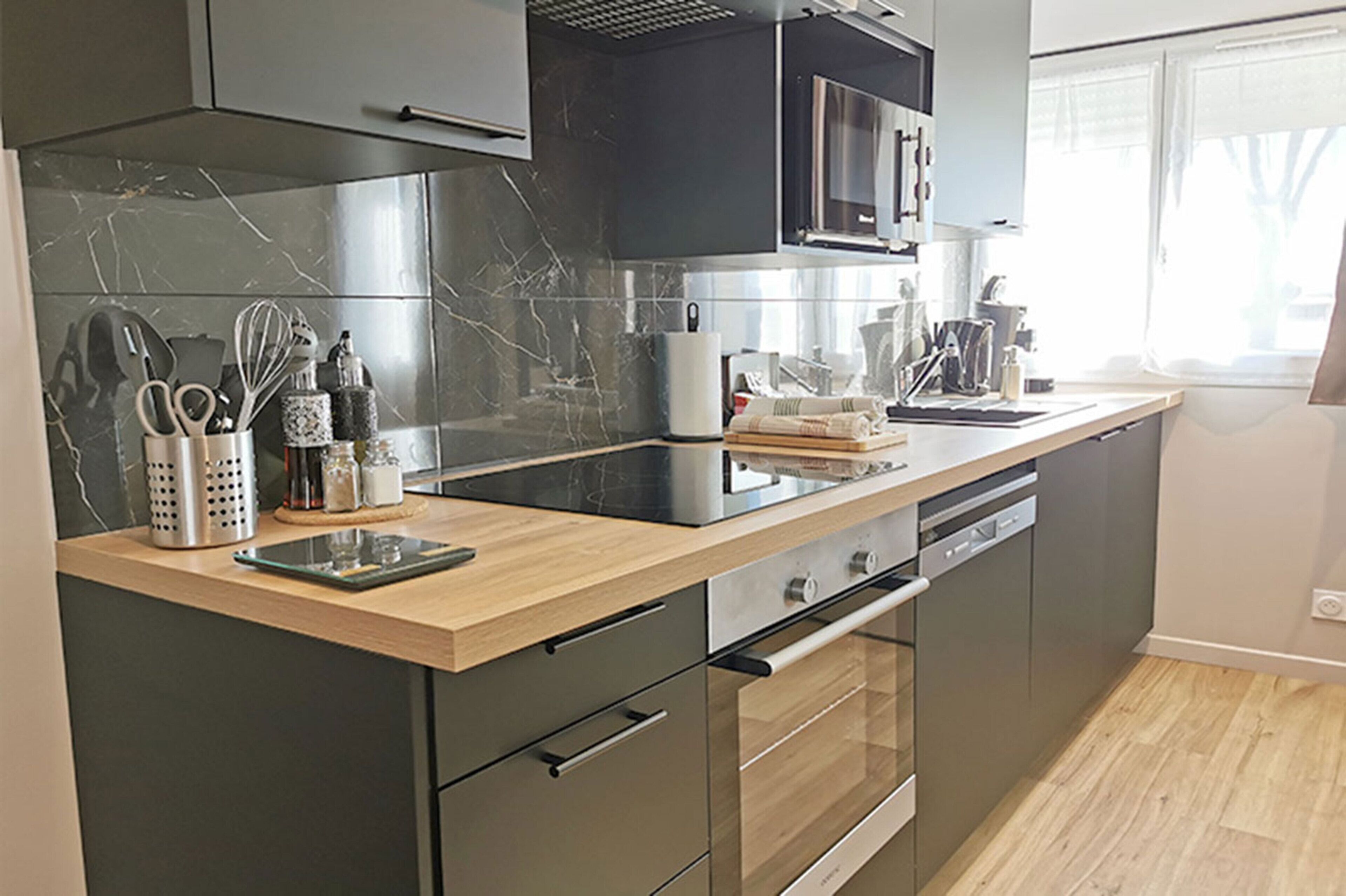 Una cocina moderna con armarios oscuros, encimera de madera y electrodomésticos de acero inoxidable.