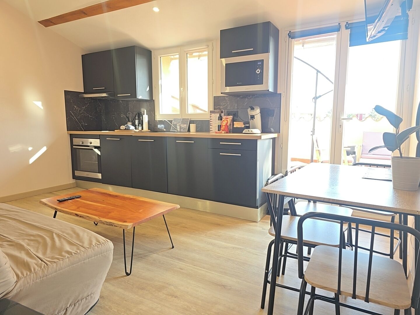 A modern kitchen with dark cabinets, a built-in oven, and a dining area with a wooden table and chairs.