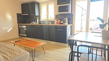 A modern kitchen with dark cabinets, a built-in oven, and a dining area with a wooden table and chairs.