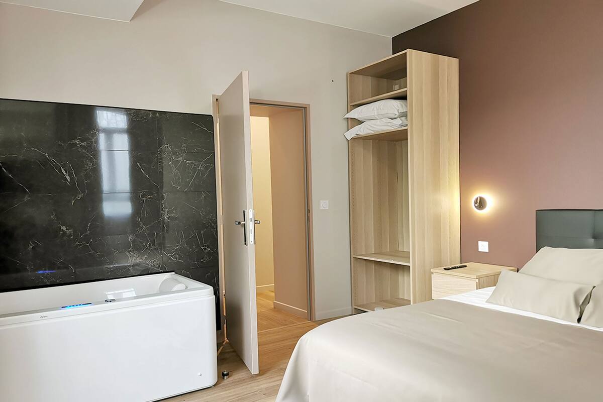 A modern hotel room with a bed, a built-in TV, a wardrobe, and a bathroom with a white toilet.