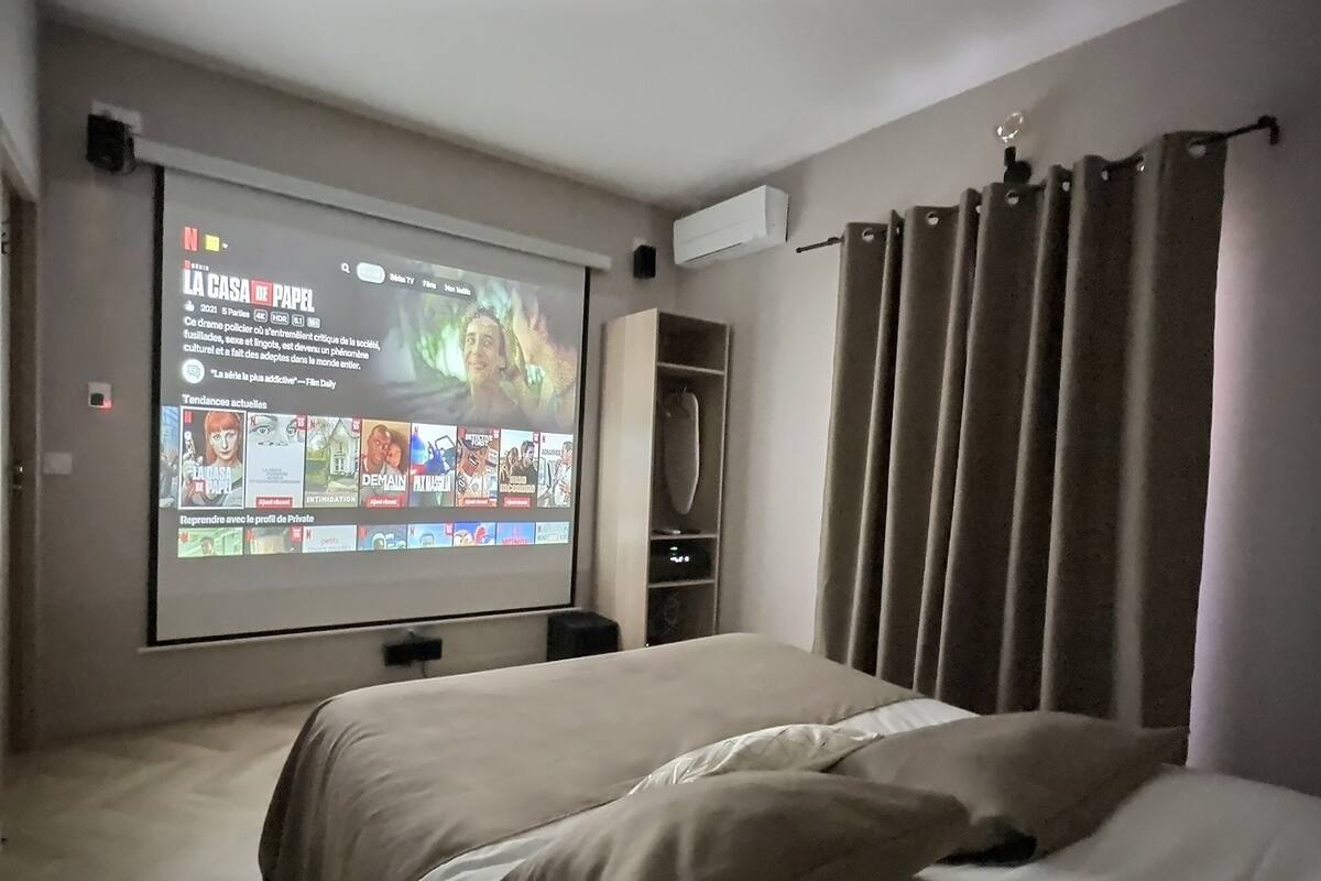 A hotel room with a bed, a TV screen displaying a movie, and a wardrobe.