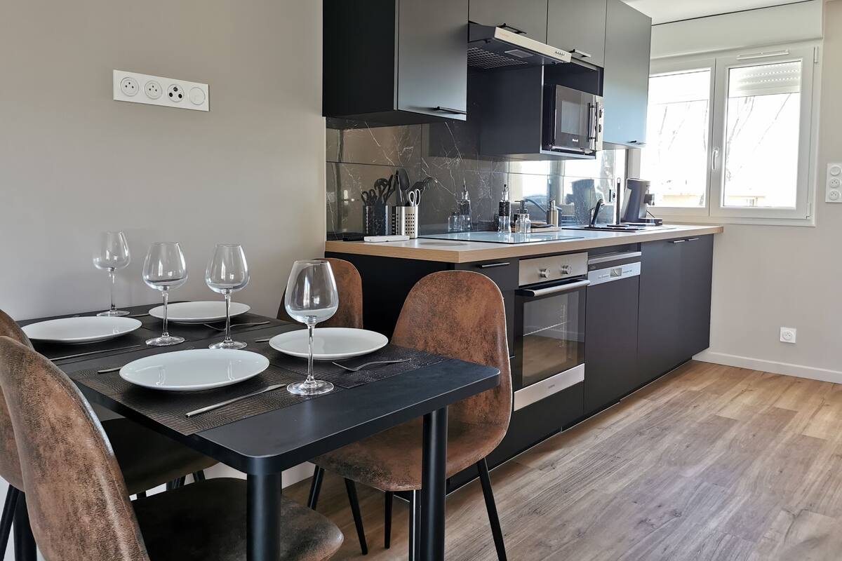 A modern kitchen with dark cabinetry, a built-in oven, and a dining area with a black table and chairs.