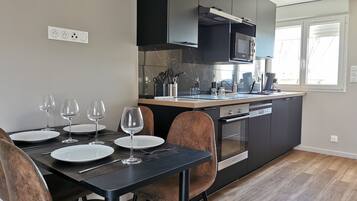 Une cuisine moderne avec des meubles de couleur sombre, un four encastré et un coin repas comprenant une table et des chaises noires.