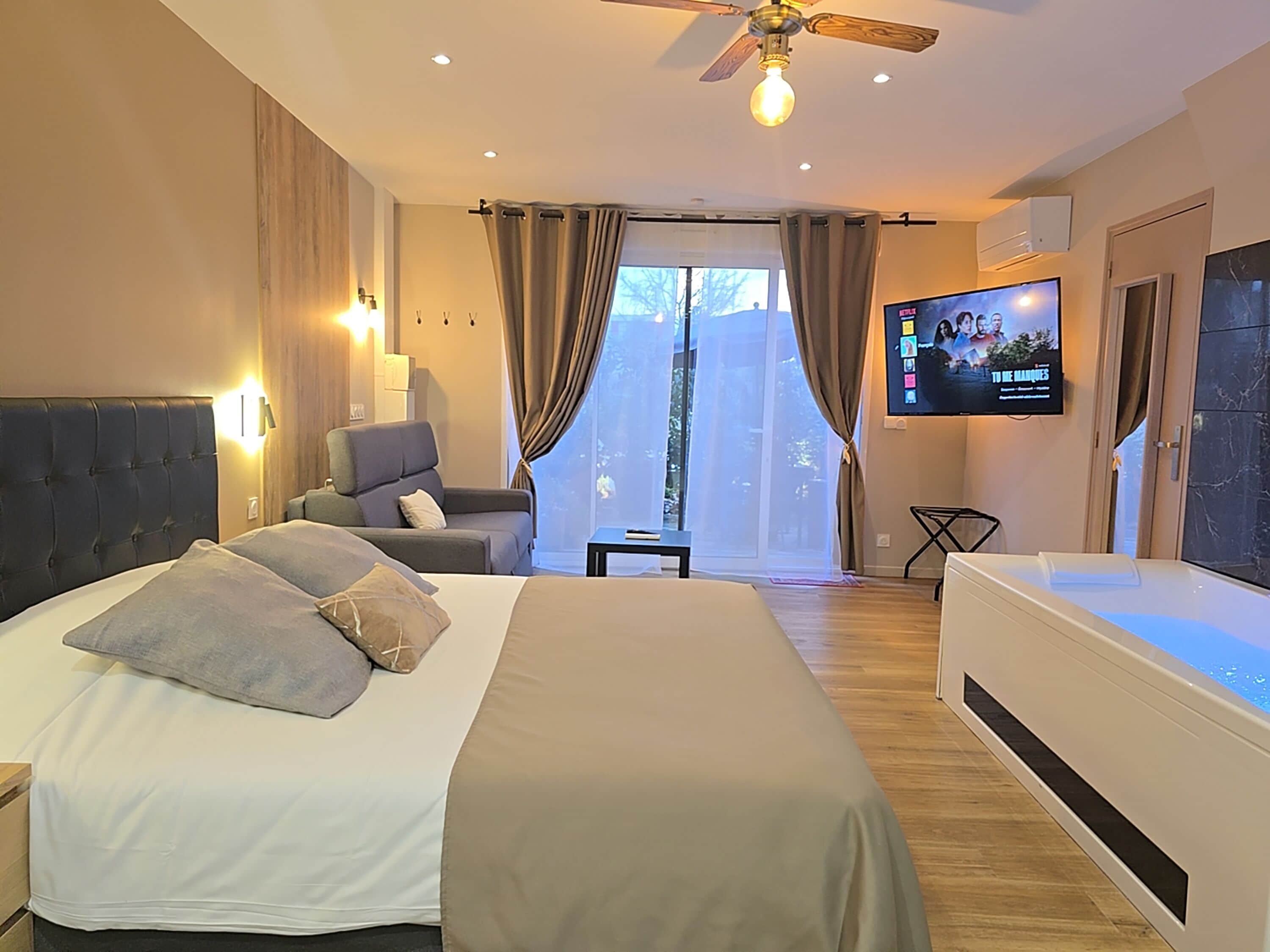 Una habitación de hotel moderna con una cama grande, un área de descanso, televisión y un balcón con cortinas.