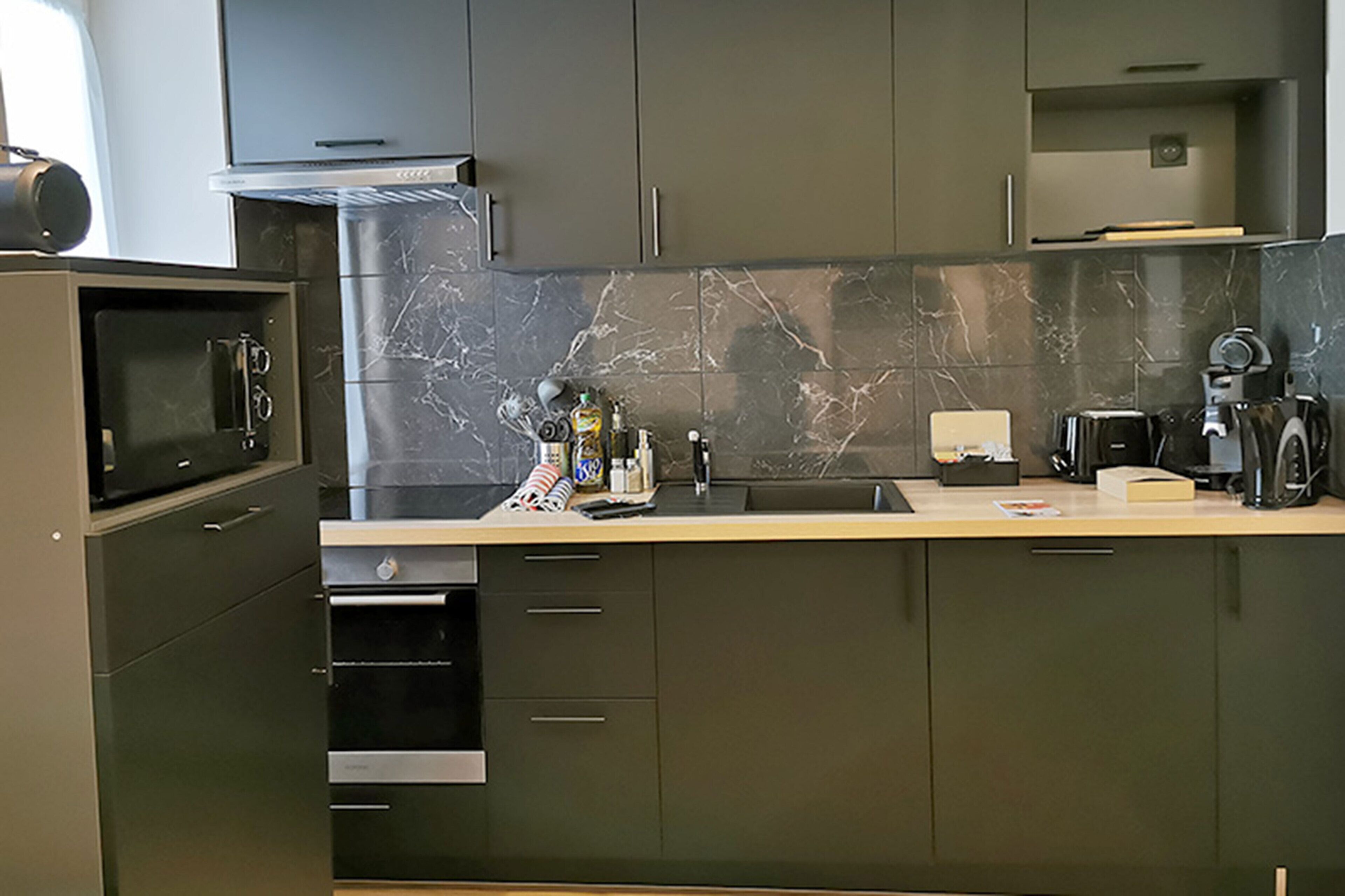 A modern kitchen with dark cabinets, a marble backsplash, and stainless steel appliances.