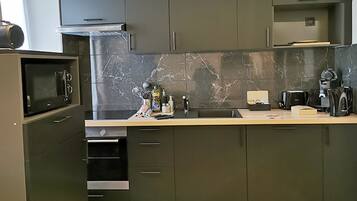 A modern kitchen with dark cabinets, a marble backsplash, and stainless steel appliances.