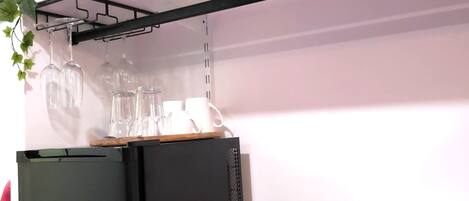 A compact kitchen area with a black refrigerator, a coffee maker, and a basket of tea bags.
