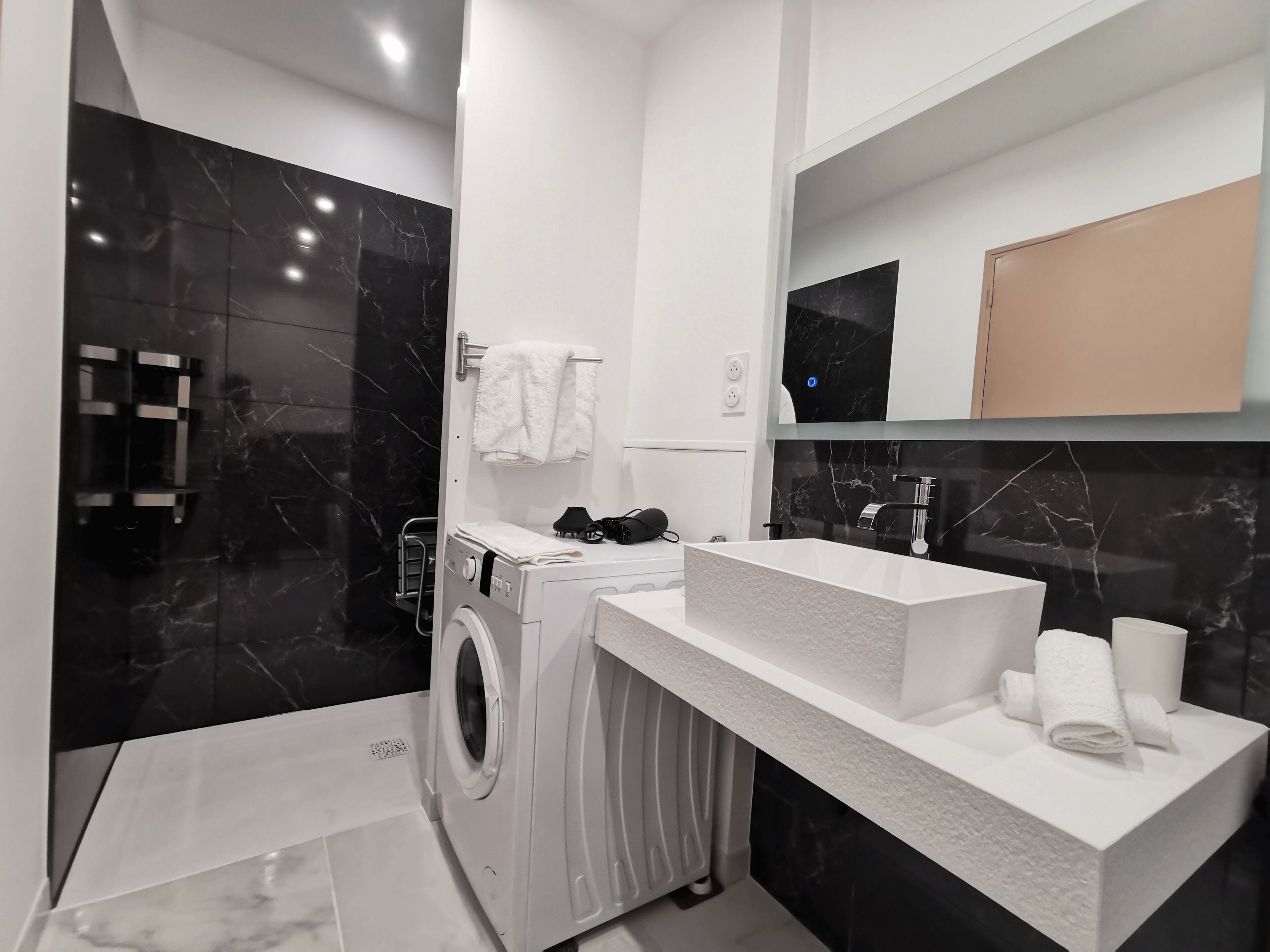 Un baño moderno con lavadora integrada, un espejo grande y un lavabo blanco.
