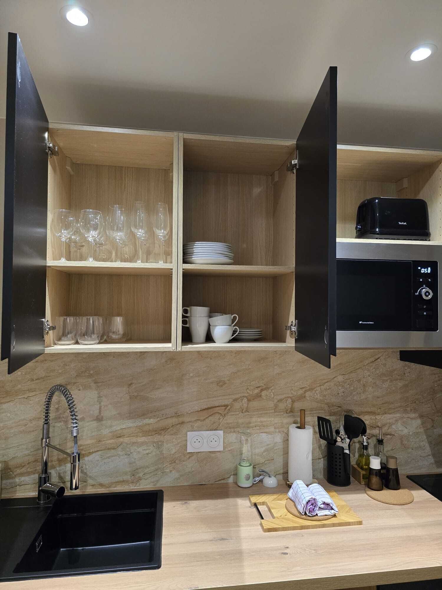 Una cocina moderna con armarios de madera, un microondas integrado y un lavamanos de acero inoxidable.