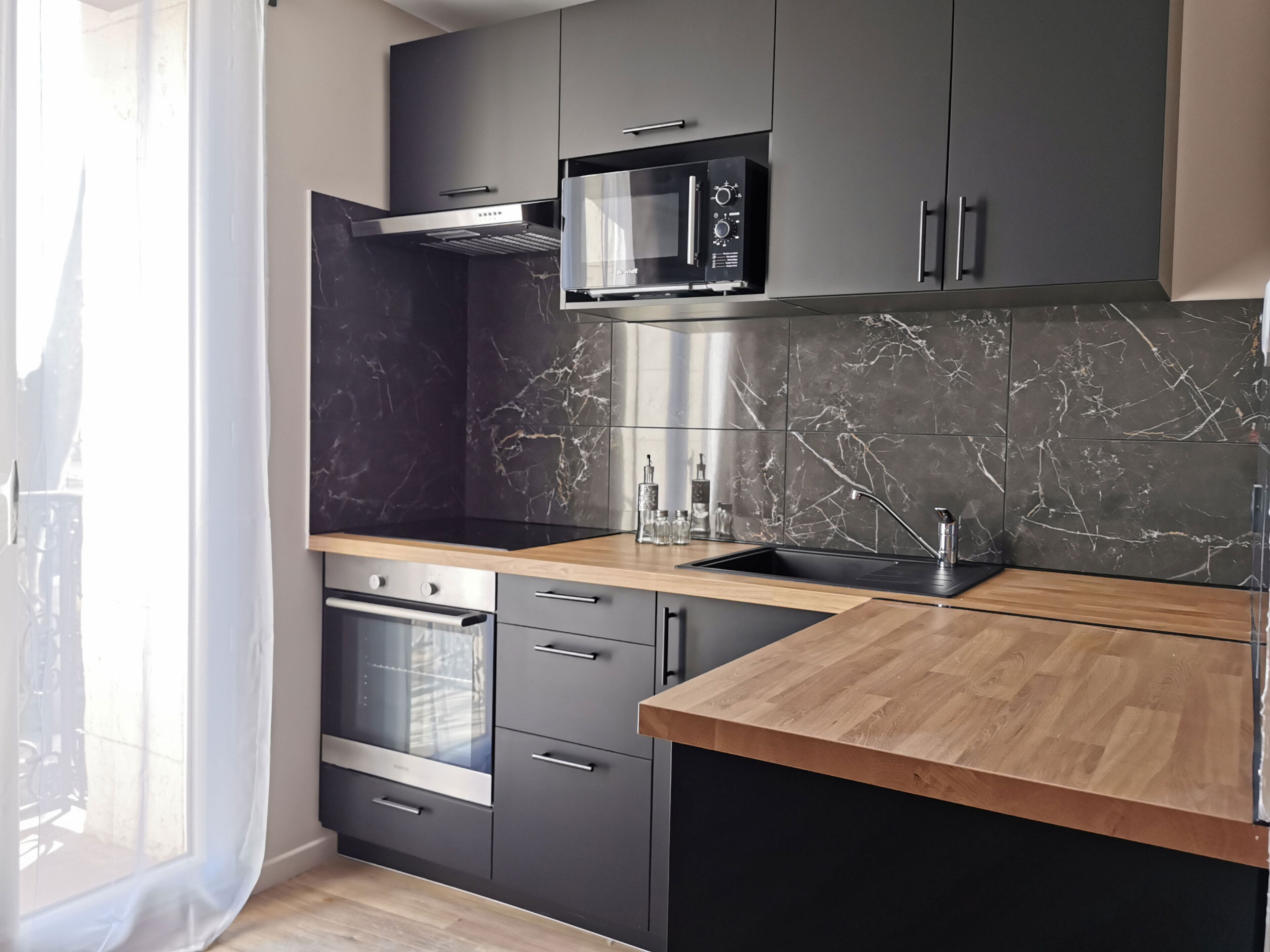 A modern kitchen with dark cabinetry, a wooden countertop, a built-in oven, and a stainless steel microwave.