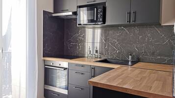 A modern kitchen with dark cabinetry, a wooden countertop, a built-in oven, and a stainless steel microwave.