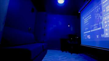 A dark room with a large screen displaying a user interface, a couch, and a small table.