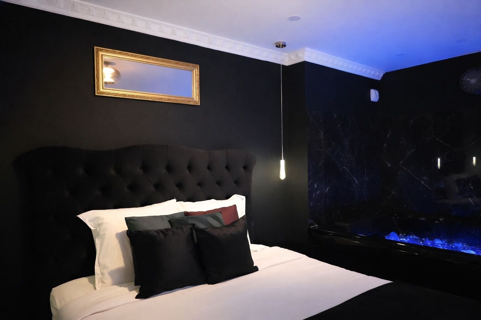A bedroom with a tufted headboard, a bed with white and black bedding, a mirror, and a large aquarium.