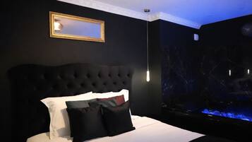 A bedroom with a tufted headboard, a bed with white and black bedding, a mirror, and a large aquarium.