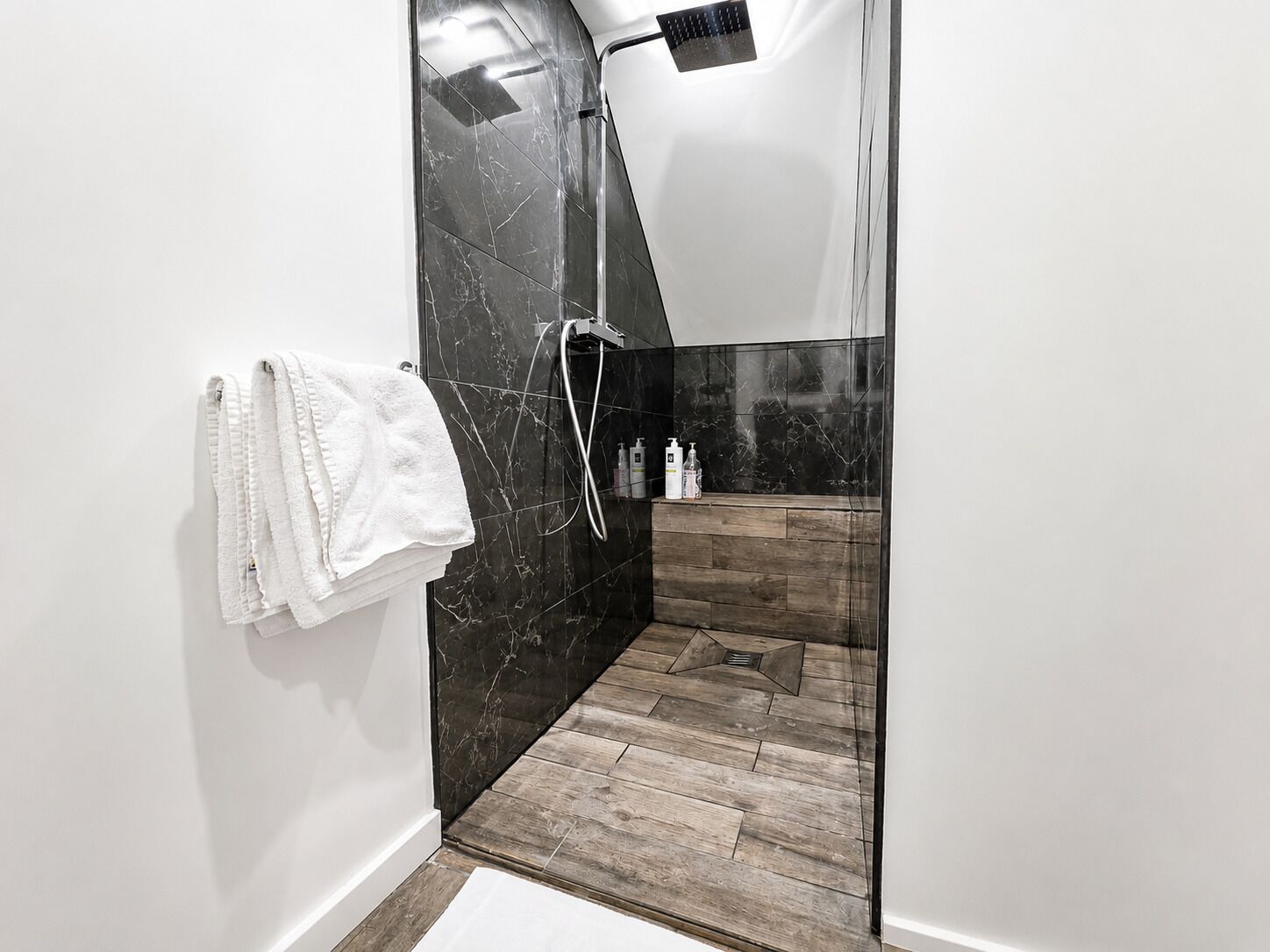 A modern bathroom with a shower, a wooden floor, and a white towel hanging on the wall.