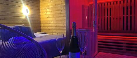 Een kamer met een bed, een tafel met champagne en twee glazen, en een stoel.