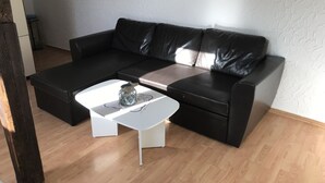 A modern living room with a black leather sofa, a white coffee table, and a small painting on the wall.