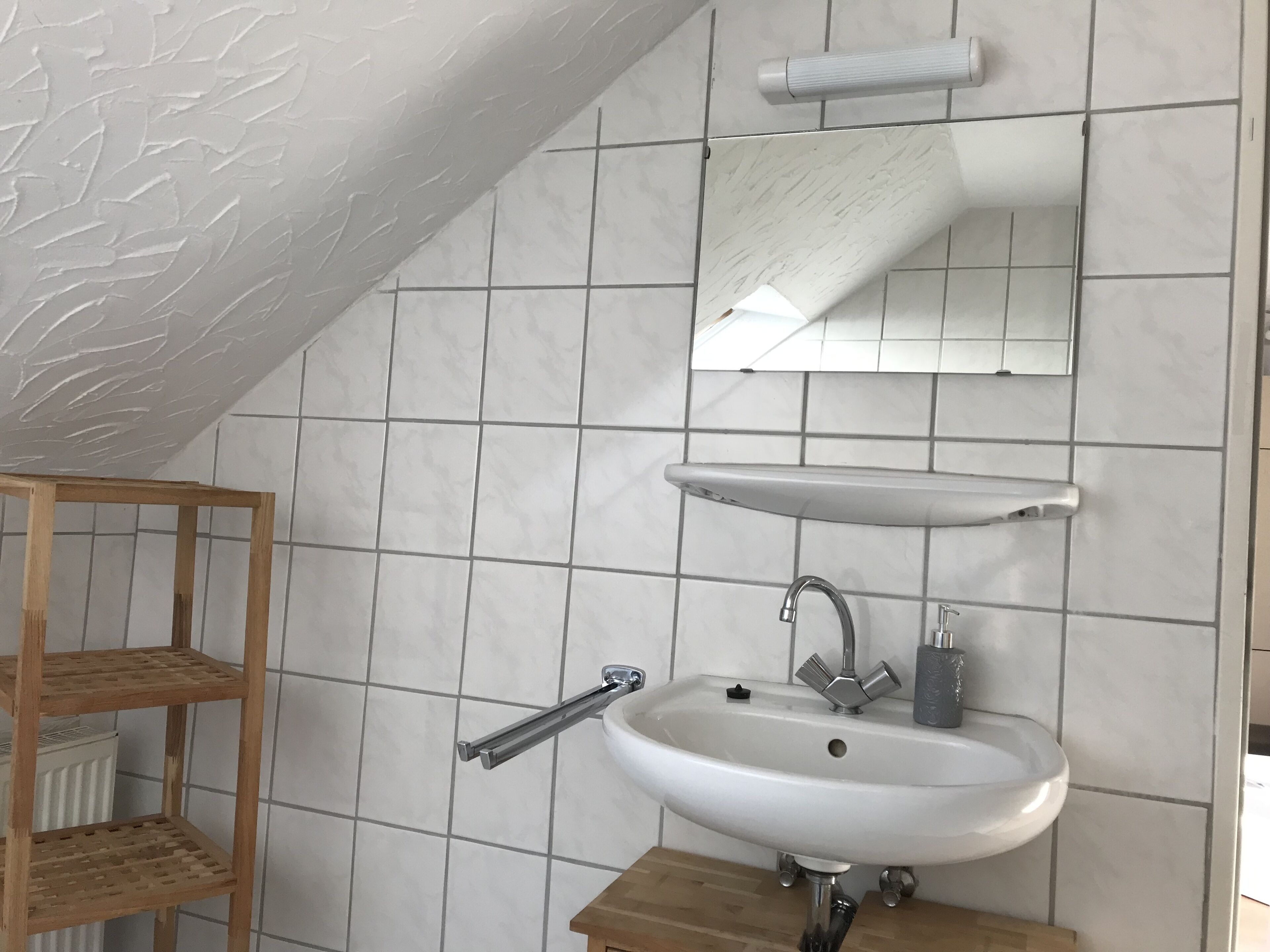 Uma casa de banho com uma pia branca, um espelho e uma estante de madeira.