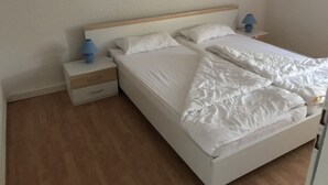 A single bed with white bedding, a wooden headboard, and a nightstand with a blue lamp.