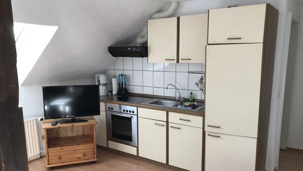 A compact kitchen with a TV on a wooden stand, a stove, and a sink.