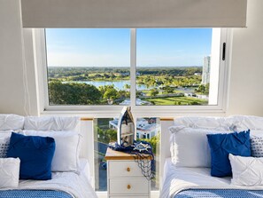A bedroom with two beds, a view of a lake and buildings, and a dresser with a ship's wheel decoration. - Family-Friendly Ocean View Apto in Playa Blanca (Coclé)