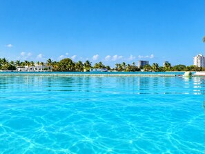 A clear blue pool with a view of a resort area, including palm trees and buildings in the background. - Family-Friendly Ocean View Apto in Playa Blanca (Coclé)