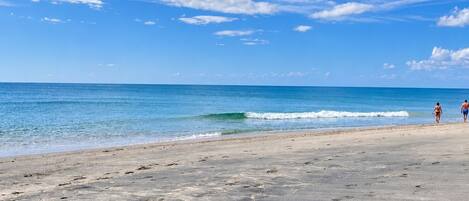 A beach with footprints leading to the water, a clear sky, and two people walking.
