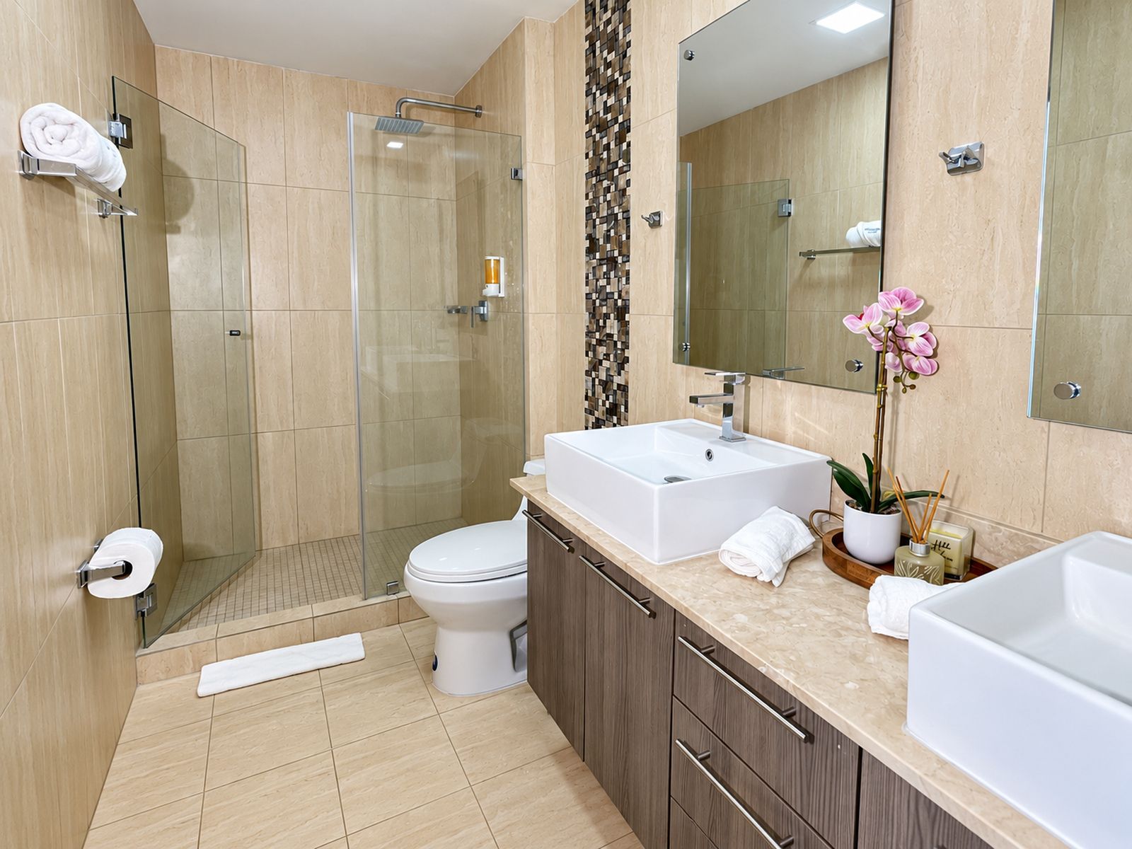 Een moderne badkamer met een douchecabine van glas, een toilet en twee wasbakken.