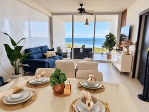 A modern living room with a dining area set for a meal, a sofa, and a view of the ocean. - Family-Friendly Ocean View Apto in Playa Blanca (Coclé)