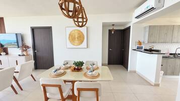 Un espace repas moderne avec une table dressée pour quatre personnes, une cuisine dotée d’un îlot central et une grande fenêtre offrant une vue dégagée.
