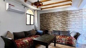 Uma sala de estar espaçosa com pé direito alto, vigas de madeira aparentes, uma grande janela, uma parede de pedra e um sofá moderno.