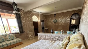 Quarto com uma cama grande, um sofá, uma parede de pedra, um lustre e uma janela com cortinas.