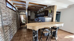 Uma sala de jantar espaçosa com uma mesa e cadeiras de mármore, uma cozinha ao fundo e vista para a sala de estar através de uma porta aberta.