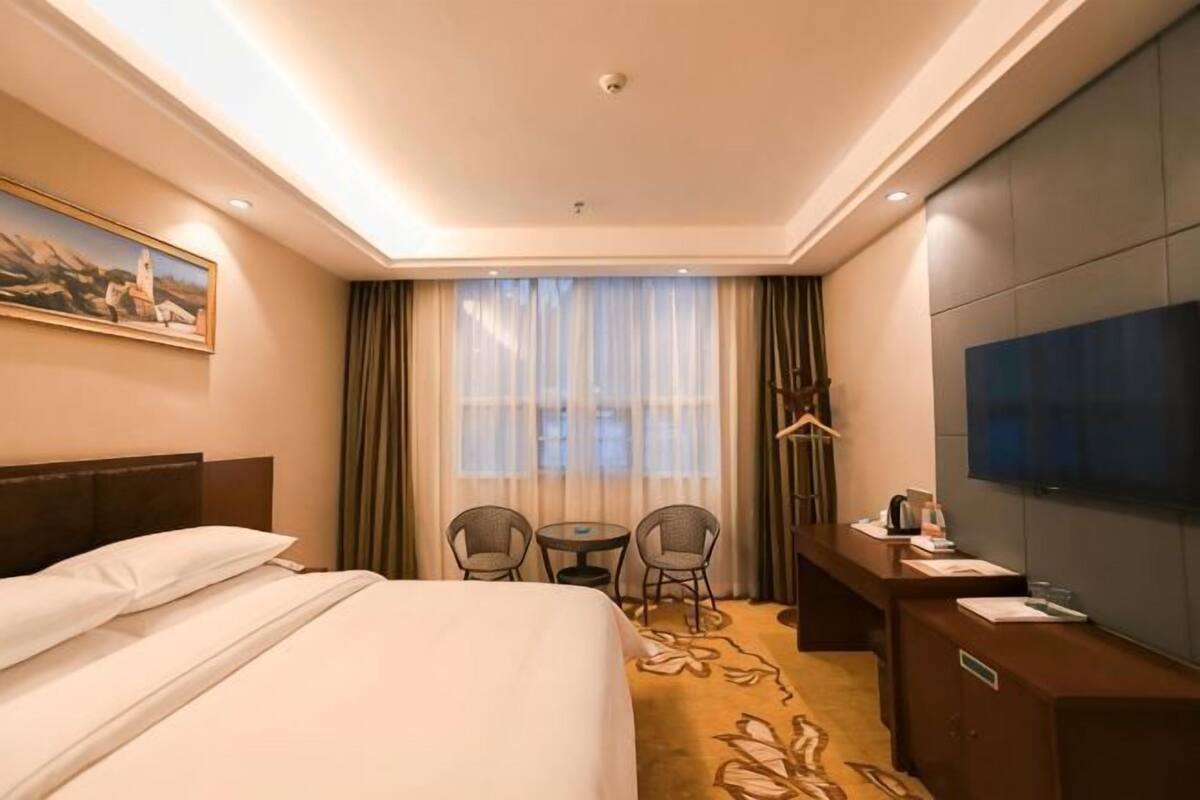 A hotel room with a bed, a desk, a TV, and a window with curtains.