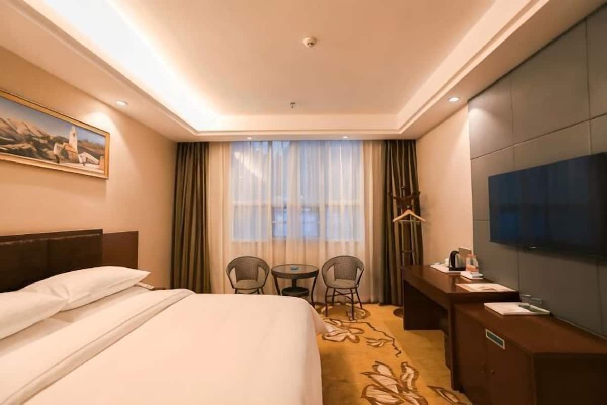 A hotel room with a bed, a desk, a TV, and a window with curtains.