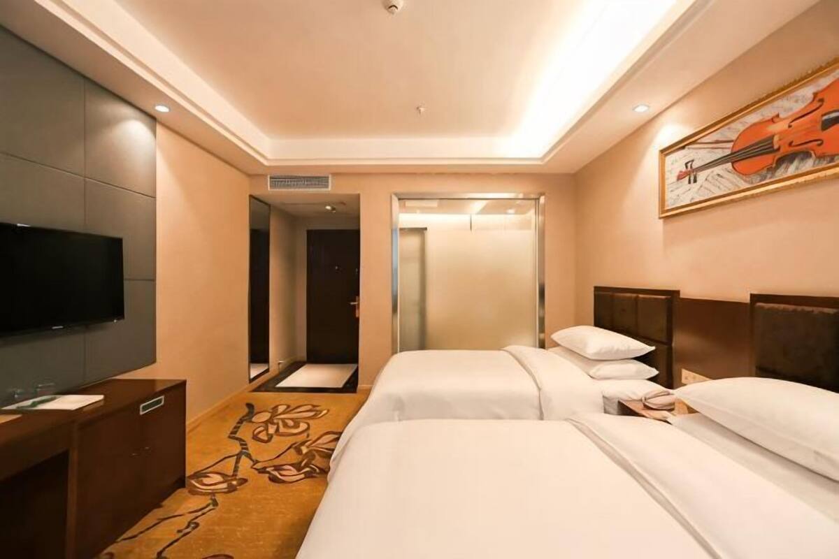 A hotel room with two beds, a TV, a mirror, and a painting on the wall.