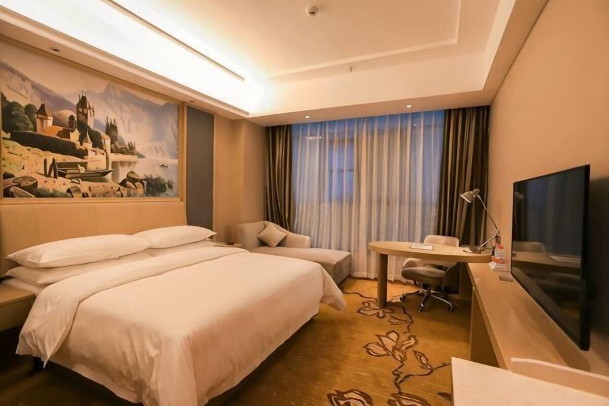 A hotel room with two beds, a desk, a TV, and a painting on the wall.