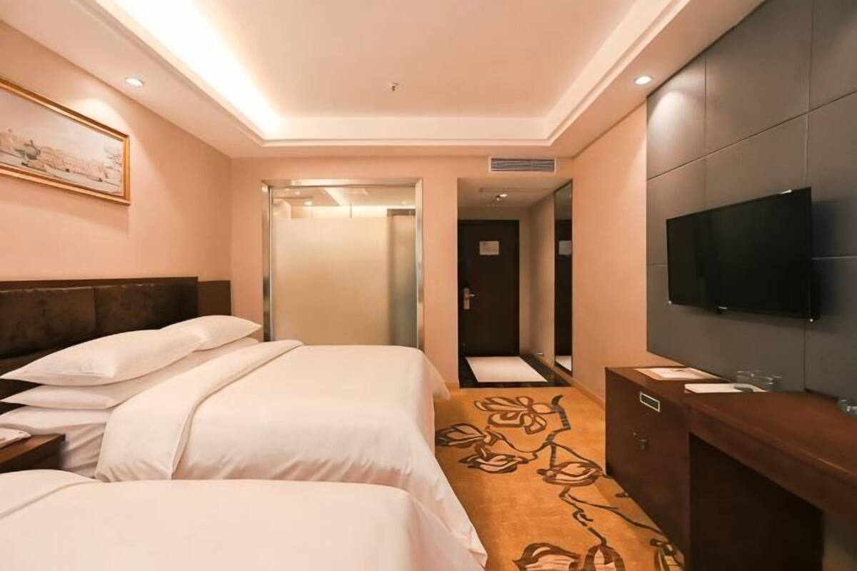 A hotel room with two beds, a TV, a desk, and a bathroom.